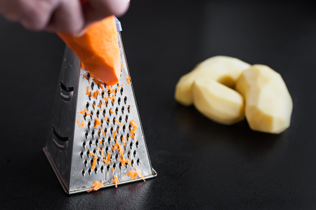 grate carrots on a grater. Potatoes in the backgroundの写真素材