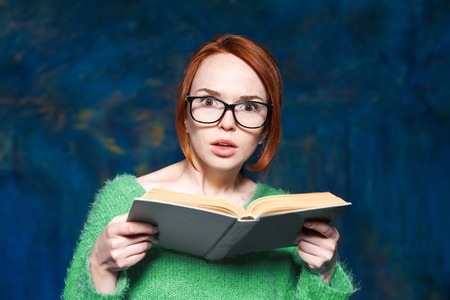 beautiful red-haired girl in a green sweater and glasses reading  bookの写真素材