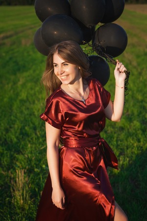 Elegant girl in red dress with black balloonsの写真素材