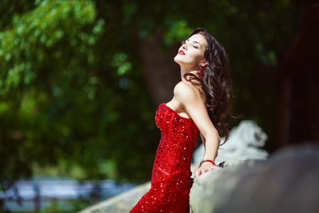 Chic woman with dark curly long hair in red dressの写真素材