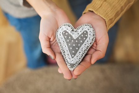Lovers hands holding handmade heart of gray sackcloth, burlap, white beads and lace. Rustic decor for home in Valentines day styleの写真素材