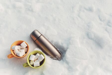 marshmallow in cup and thermos on snowの写真素材