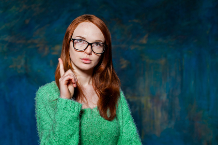 Pensive redhead girl shows finger with arms akimboの写真素材