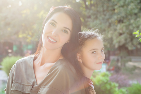 Young mom and daughter sitting back to back in park on sunny dayの写真素材