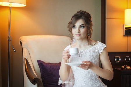 Attractive bride preparing for wedding in the morning, drinking hot tea and waiting for the groomの写真素材