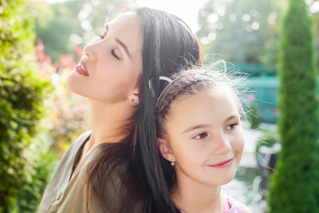 Young mother sitting with closen eyes back to back with daughter in beautiful nature. Concept of happy familyの写真素材