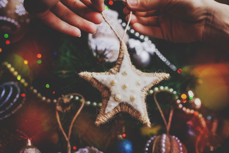 Hipster hands with Christmas sackcloth star and tree background. xmas decorations with toys, sparkling, glowing. Happy New Year and Xmas themeの写真素材