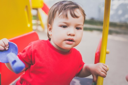 portrait of little boy in red t-shirt excitedly playing on playground. concept of happy healthy childの写真素材