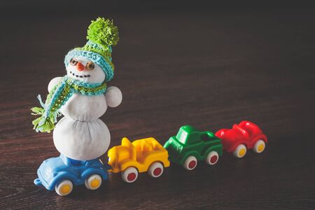 Christmas hipster snowman in green hat and scarf and color cars model on wooden background with copyspace. concept of happy new year and merry xmas giftの写真素材