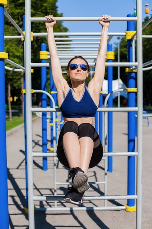 Young athletic woman trainer in a bright blue sport bra, black leggings and dark sunglasses making...