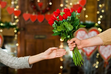 Close up shot of male hand holding flowers. Only hands with flowers over valentines day decorationの写真素材