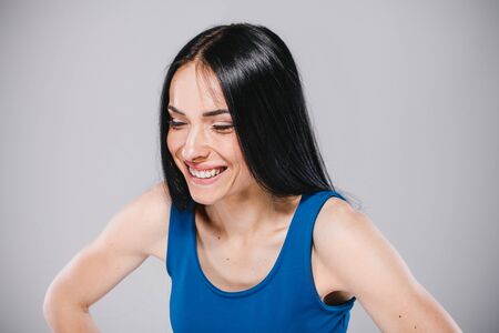 young teenager with long brunette hair in blue dress smiling in photostudio on gray backgroundの写真素材