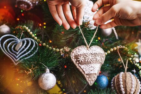 hands with Christmas sackcloth heart and tree background. xmas decorations with toys, sparkling, glowing. Happy New Year and Xmas theme for postcardの写真素材