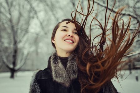 portrait of beautiful young teenager with long brunette hair in fur coat smiling and spending time outdoors in the winter forest.の写真素材