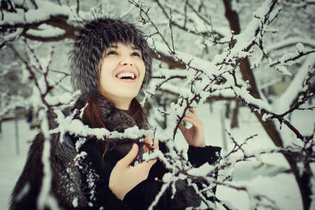 portrait of beautiful young woman in fur coat and fur hat smiling and spending time outdoors in the winter forest.の写真素材