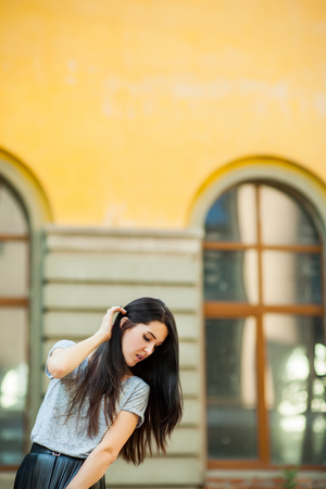 young lady posing near building. sweet woman in a gray shirt and a black leather skirt walking around city. Concept of modern freedom hipster humanの写真素材