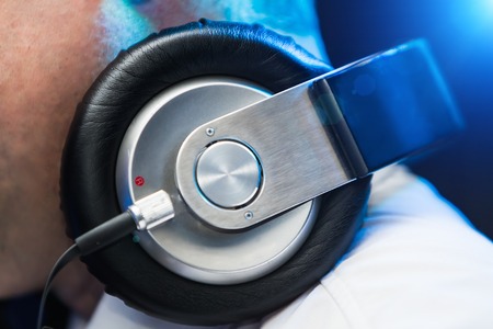 Close up photo of headphones on a DJ wearing white shirt playing music at nightclub.の写真素材