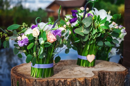 two bunches of beautiful wedding bouquets of fresh flowers tied with ribbons standing on wooden stump near the lake and trees on the countrysideの写真素材