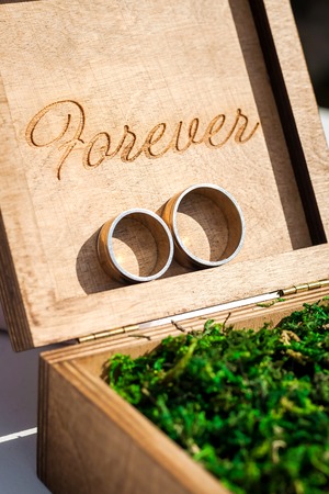 two beautiful golden bridal rings lying in a wooden box with engraving filled with moss.の写真素材