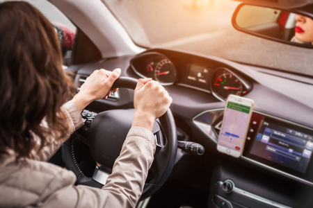 young beautiful woman with red lips being seen in a mirror keeping the steering wheel of a vehicle and driving attentively.の写真素材