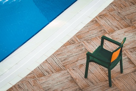 Comfortable green plastic chair at the clean cool swimming pool with blue water of the luxury hotel...