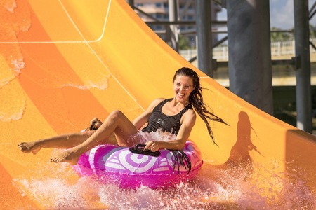 pretty woman on the rubber ring having fun on the orange water slide in the aqua park.
