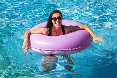 pretty happy woman with slim figure in black bikini holding rubber ring in the swimming pool.