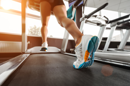 close up woman's feet running on the treadmill at the gym over sunrise. wearing in white orange blue sneakers.の写真素材