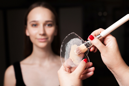 makeup artist blending the mixed foundation on a glassy surface with a brush before applying it on a face of a young beautiful woman. concept of natural make upの写真素材