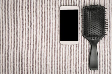 hairbrush lying near a mobile phone on a grey striped cloth. concept of modern hairdresser tools. free space for textの写真素材