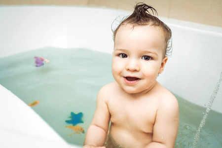 Cute happy little child with strange hairdo taking bath with color toys. Concept of childs hygiene, healthy lifestyle, carefree childhoodの写真素材