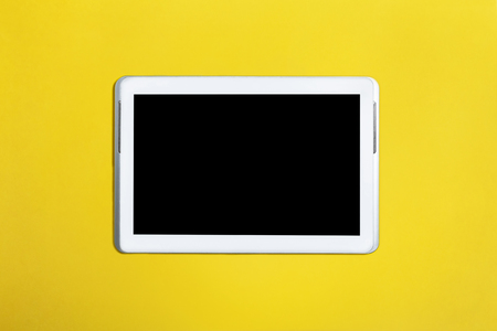 Tablet pc computer with black screen lying isolated on a yellow surface. top view. concept of modern gadgetsの写真素材