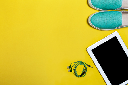 inherent parts modern persons everyday life. blue slip on shoes, green earphones and a tablet. Concept of summer sale and shopping. Top view. free space for textの写真素材