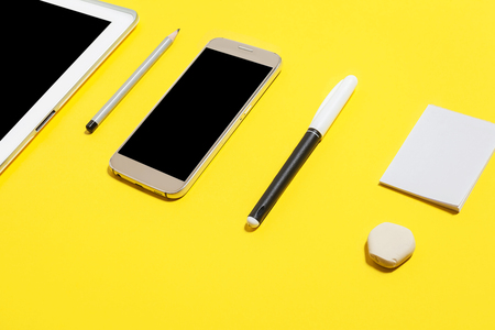 felt pen, pencil, rubber and paper stickers lying near smartphone and tablet pc at the yellow background. concept of office or educational chancery and gadgetsの写真素材