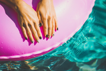 woman manicured hands laying on the rubber ring in the swimming pool. Summer Vacation. Enjoying suntan. Weekend on resortの写真素材
