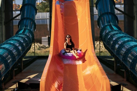pretty woman in black bikini getting down on the inflatable ring by the slide in the aqua park. Summer Vacation. Enjoying suntan. Weekend on resortの写真素材