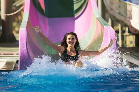 pretty brunette slim woman with spreading hands on the rubber ring having fun coming down on the purple water slide in the aqua park. Summer Vacation. Weekend on resort