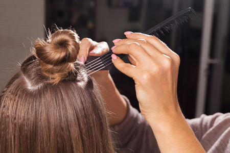 professional hairdresser making a coiffure with a bun to a young woman using different brushes in a beauty salon. concept of carefull hair treatingの写真素材