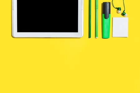 business or education accessories. green pencils, headphones, paper stickers, markers and tablet pc lying on a yellow background. concept of the office stationary and gadgets. free space for textの写真素材