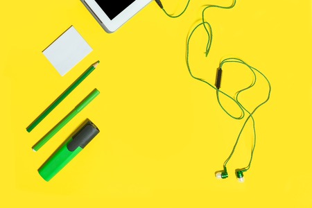 collection of educational accessories and gadgets from the top view. green pencils, headphones, paper stickers, markers and tablet pc lying on a yellow background. free space for advertising textの写真素材