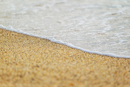 close up photo of the orange grainy sand rippled by the wind with footprints left by the visitors of the beach and foamy tideの写真素材
