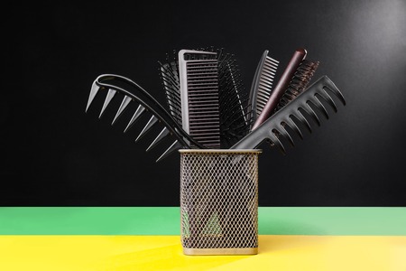 metal basket with various hairbrushes standing on a green amd yellow surface at a black lightened background. concept of professional hair caring tools. free space for advertisingの写真素材