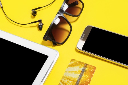 tablet pc, smartphone, earphones and sunglasses lying on a yellow background. concept of contemporary gadgets and accessoriesの写真素材