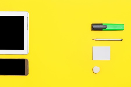 green bright marker, pencil, rubber and paper stickers lying against smartphone and tablet pc at the...