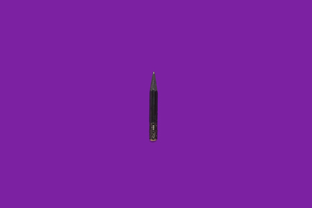 Black small used pencil lying isolated on a purple background. concept of office and educational chanceryの写真素材