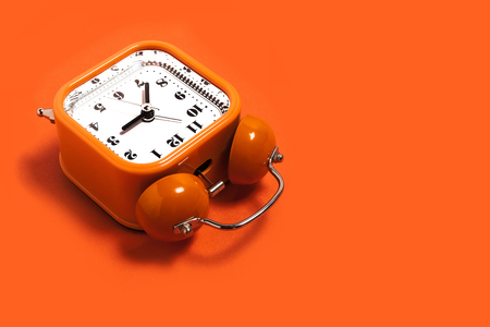 Vintage style orange metal alarm clock with bells lying on the orange surface isolated. back to school concept. free space for advertising textの写真素材