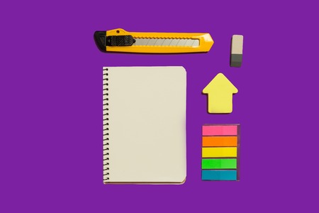 opened notebook, colorful stickers and stationary knife lying on a purple surface. concept of educational chanceryの写真素材