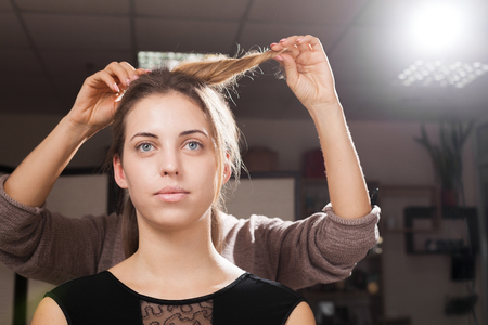 professional hairdresser making an unusual hairdo to a brown haired young model in a beauty salonの写真素材
