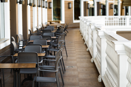 line of modern and comfortable tables and chairs in the restaurant balcony with classic white fence and big light windowsの写真素材