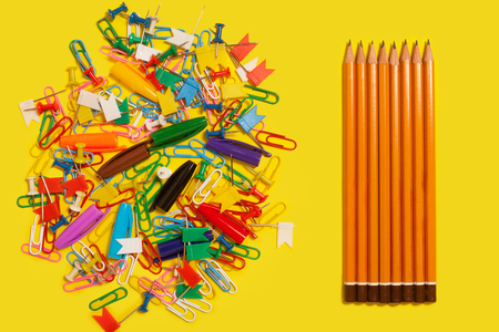 collection of colored pushpins, paper clips and pen caps lying near a row of pencils on a yellow backgroundの写真素材